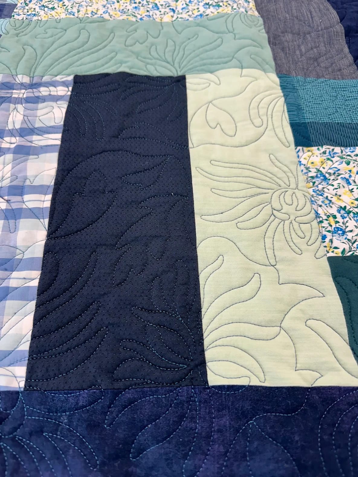 A blue and green quilt featuring a floral pattern, representing the theme of transforming memories through quilting.